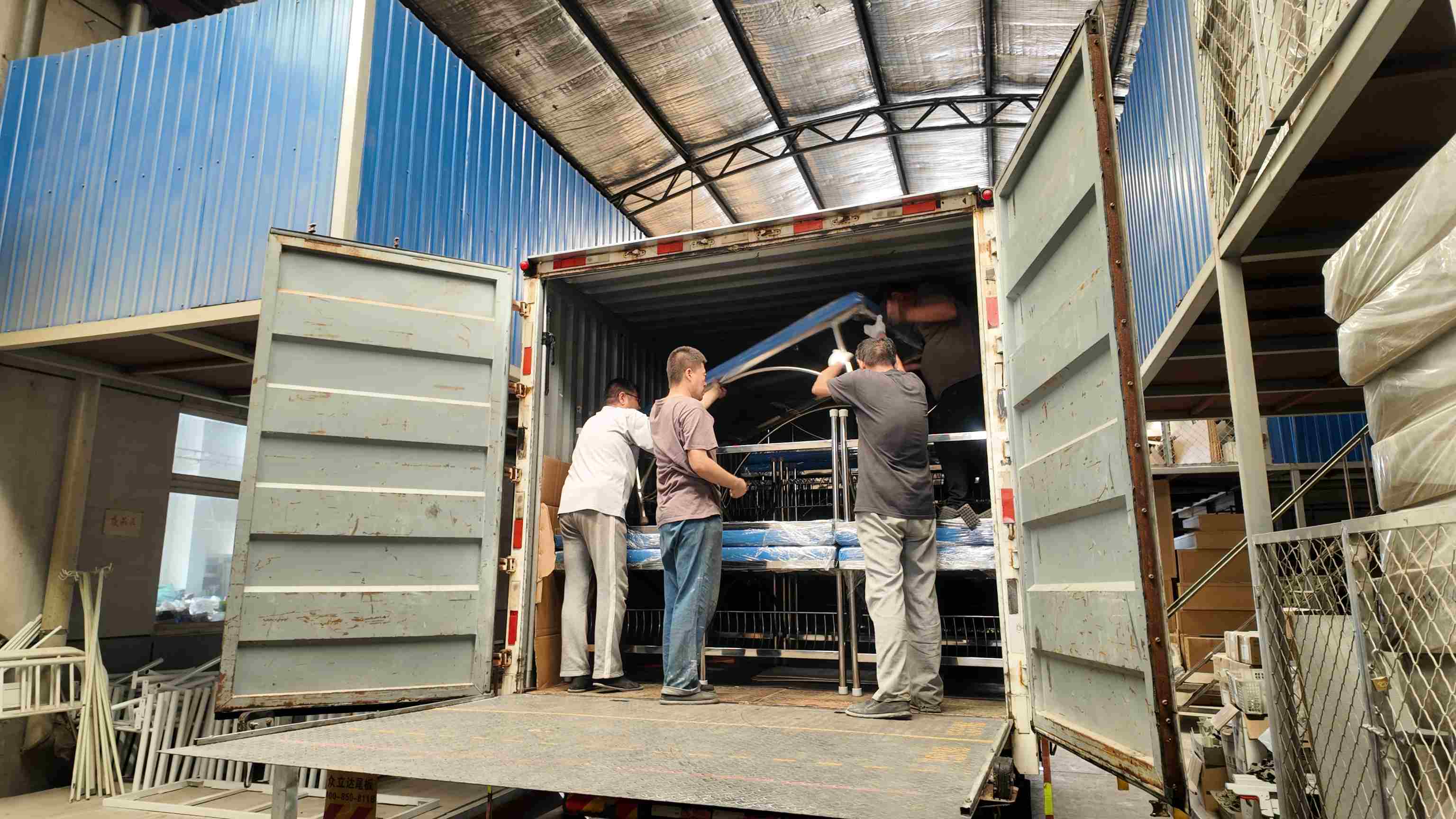 Pekerja sedang mengangkut dan memuat tempat tidur pemeriksaan ke dalam kendaraan.